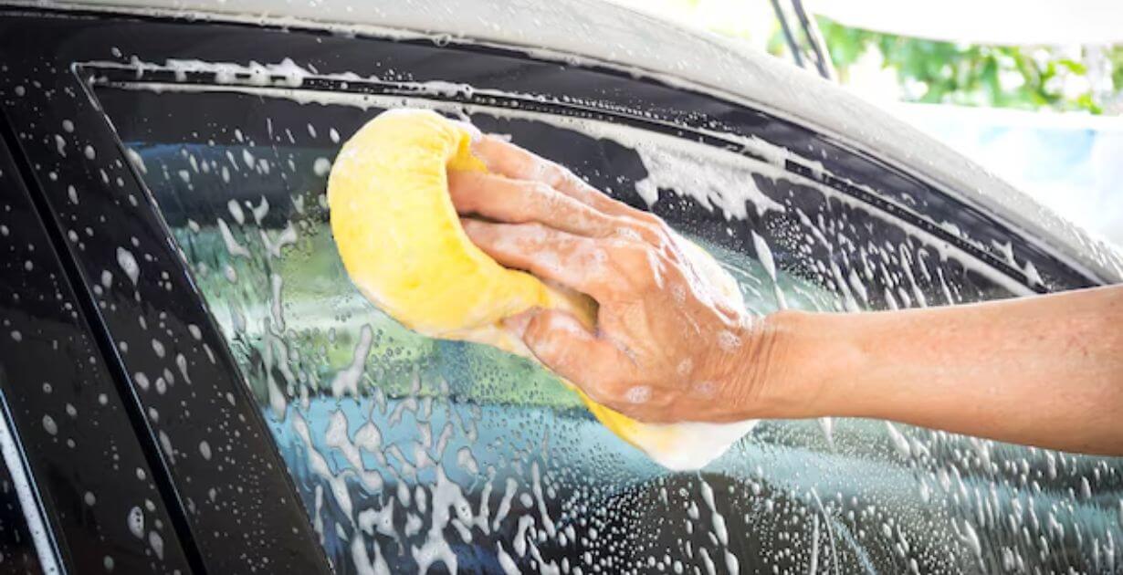 uma-pessoa-lavando-o-para-brisa-com-agua-e-bucha